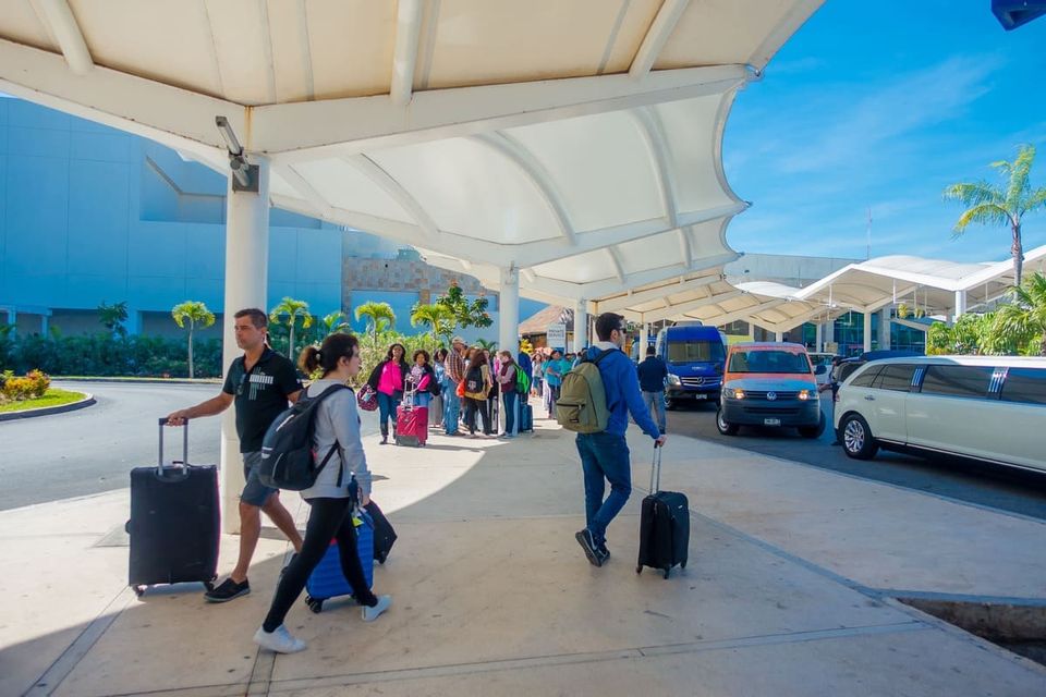 Traveler with a suitcase waiting at the airport curb, checking a ride-hailing app on a phone